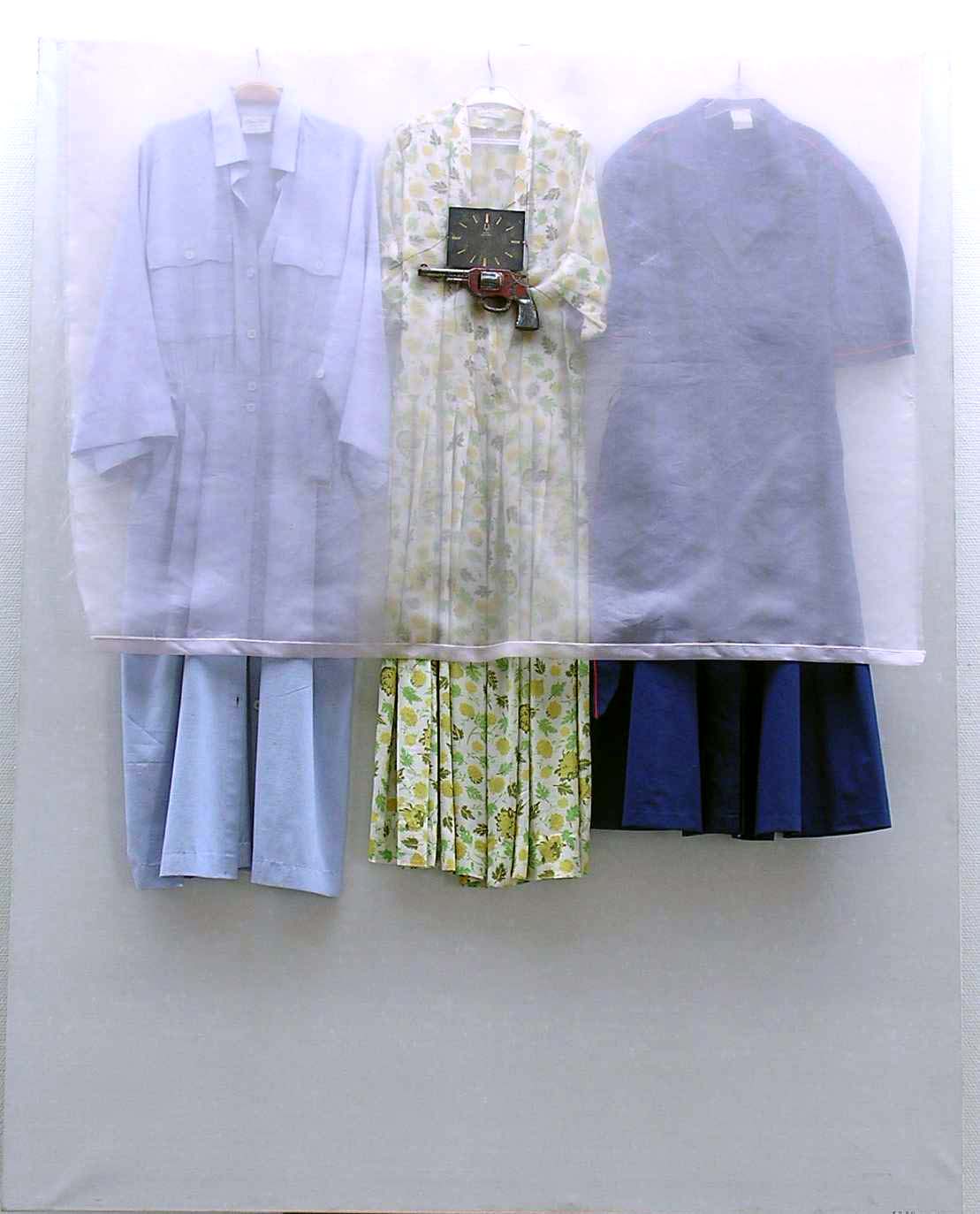 fotografi av tre klänningar som hänger på galgar och är övertäckta av ett tunt tyg, på tyget finns en pistol monterad