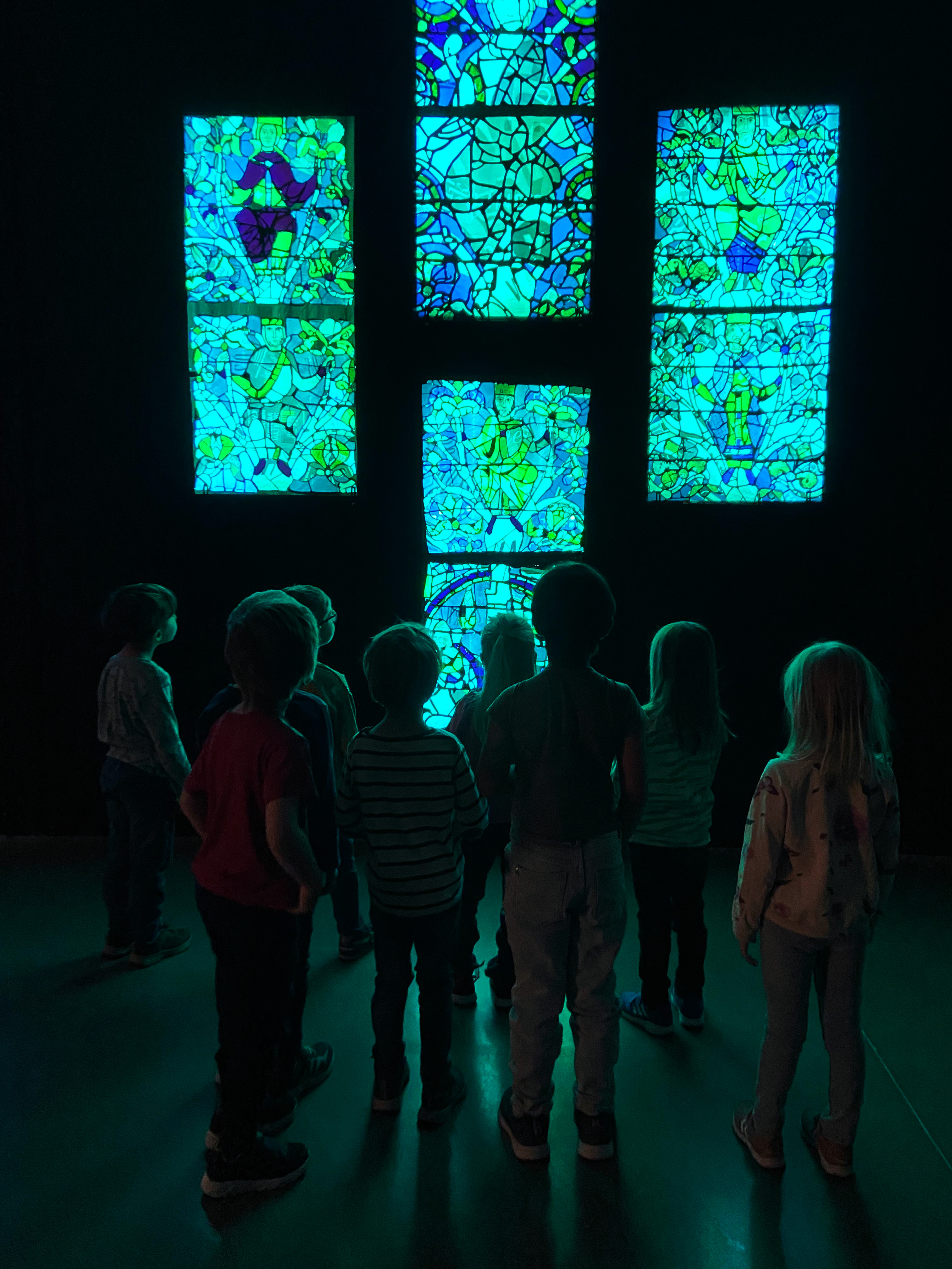 barn i 5-årsåldern står i ett mörkt rum och tittar upp mot ett upplyst konstverk som föreställer ljuslådor med mosaik med olika motiv