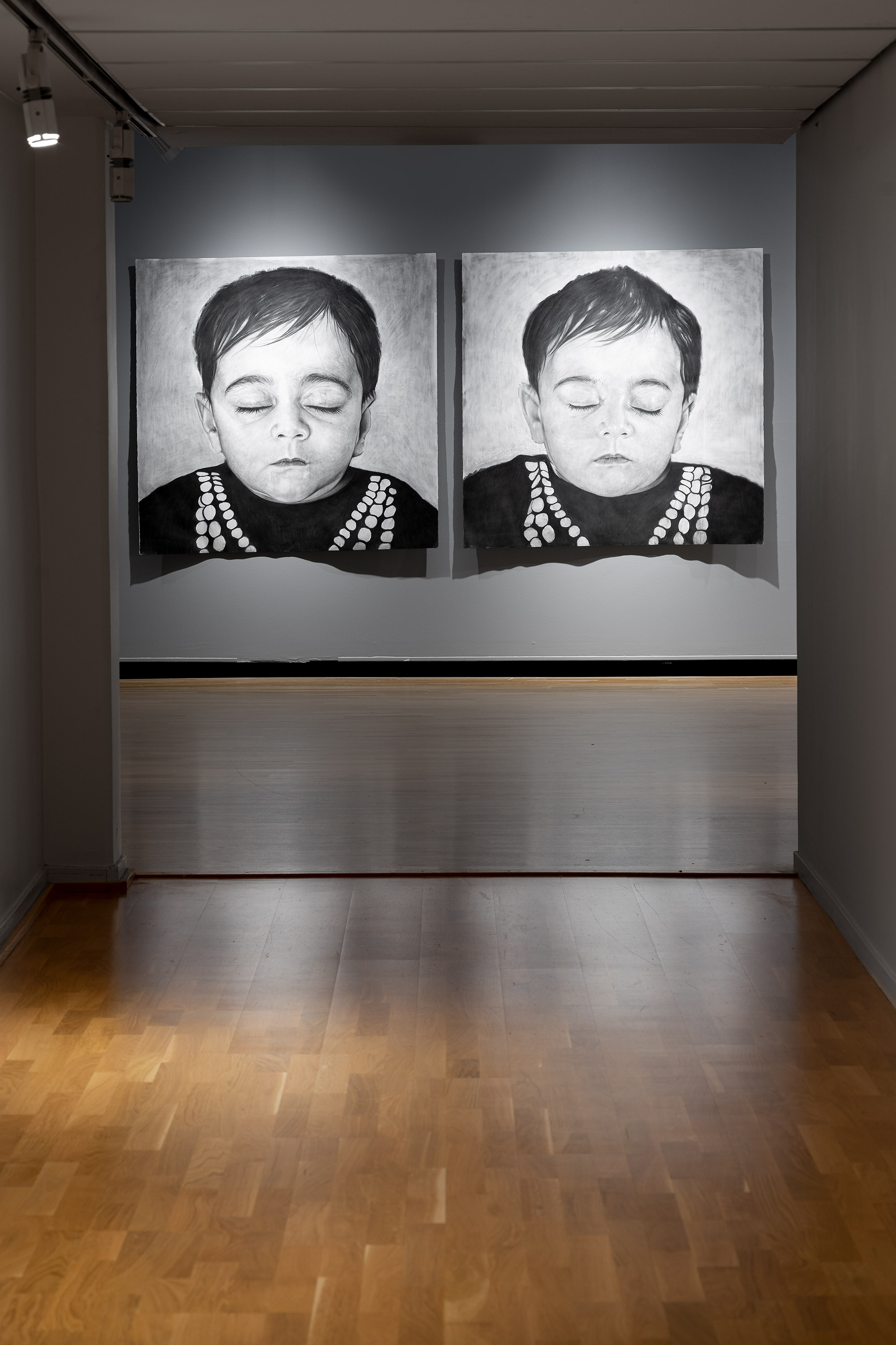 foto av ett rum med grå väggar där två stora blyertsteckningar hänger. motiv av två ansikten av barn i 2års-åldern som blundar