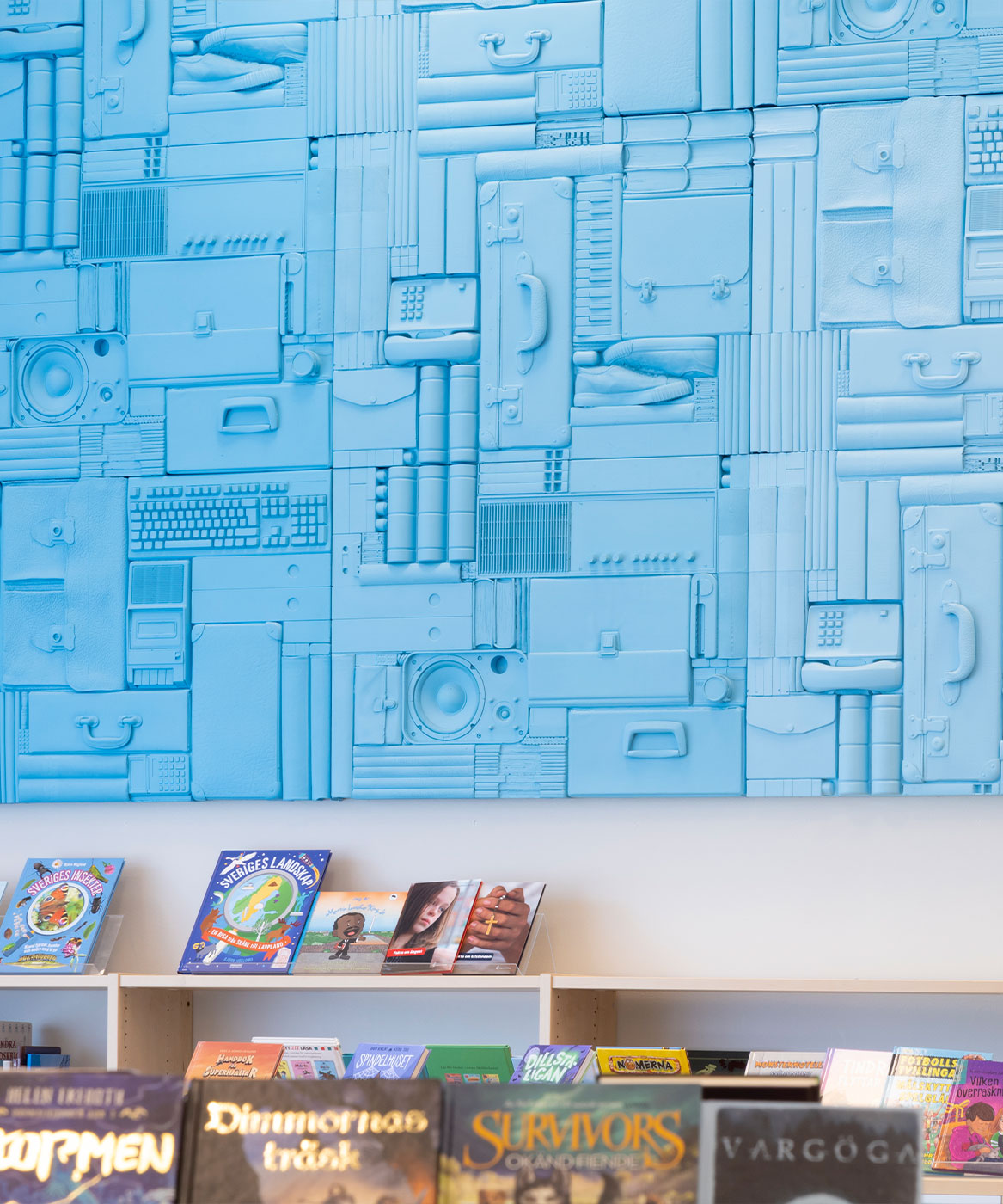 en vägg i ett bibliotek är täckt av saker som portföljer, telefoner och bokryggar, allt färgat i samma ljusblå färg