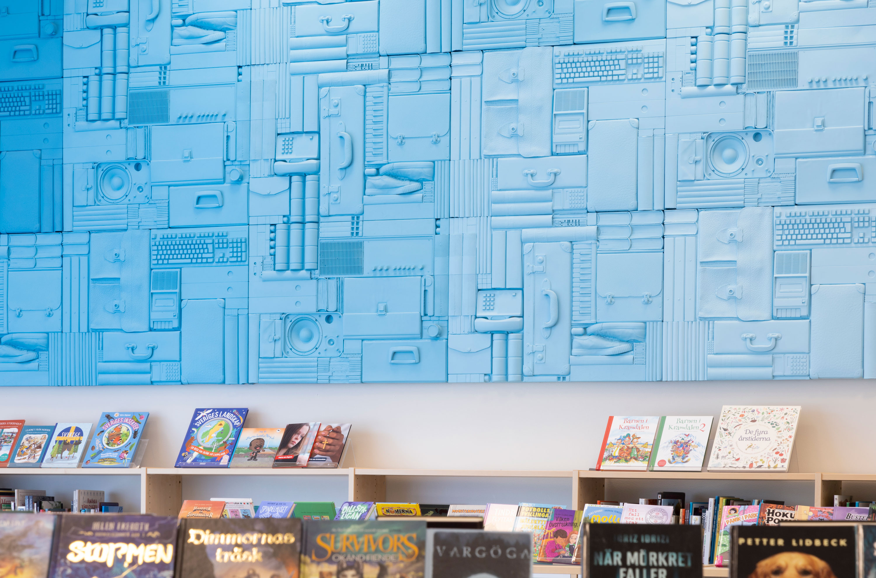 väggrelief i en färgskala från blått till vitt, med ett urval avgjutna föremål som tillsammans utgör ett upprepat mönster som löper längs en vägg