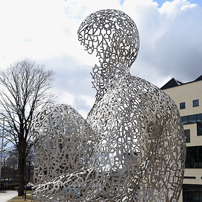 8 meter hög skulptur föreställande en hukande människofigur gjord av silverfärgade bokstäver.