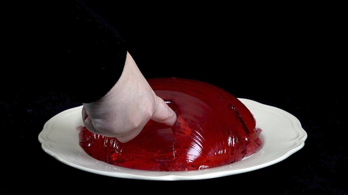 tallrik med röd jelly och en hand som petar in ett finger i jellyn
