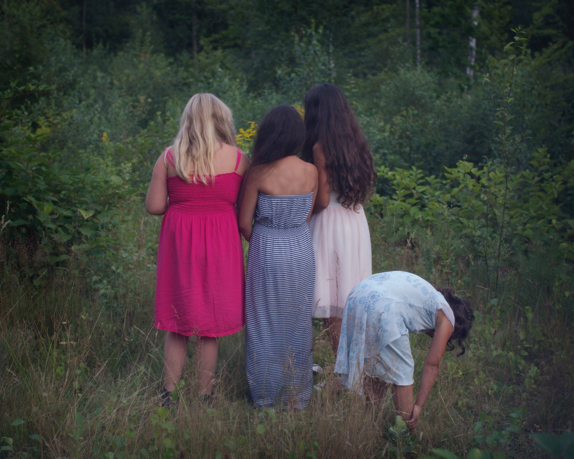 foto föreställande fyra flickor i sommarkläder i en skogsdunge som tittar bort från kameran
