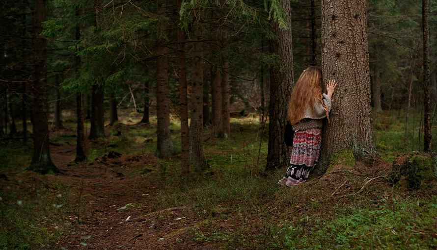 foto av kvinna som lutar huvudet mot ett träd i skog