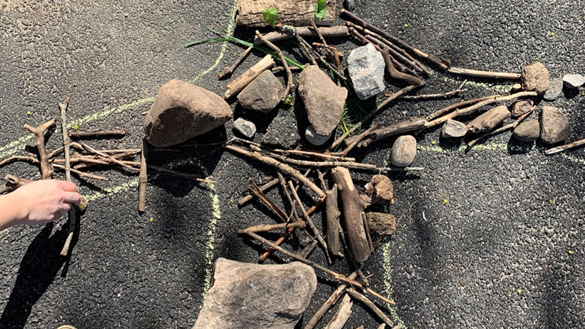 foto av asfalterad mark där en barnhand lägger pinnar och stenar i en formation