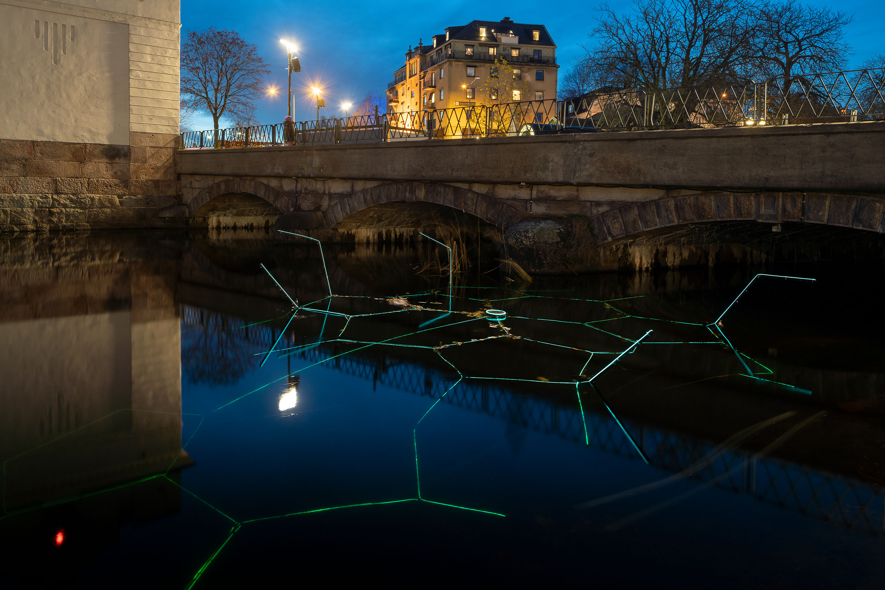 Kvällsmörker i stadsmiljö med en blå molekyl i vattendrag