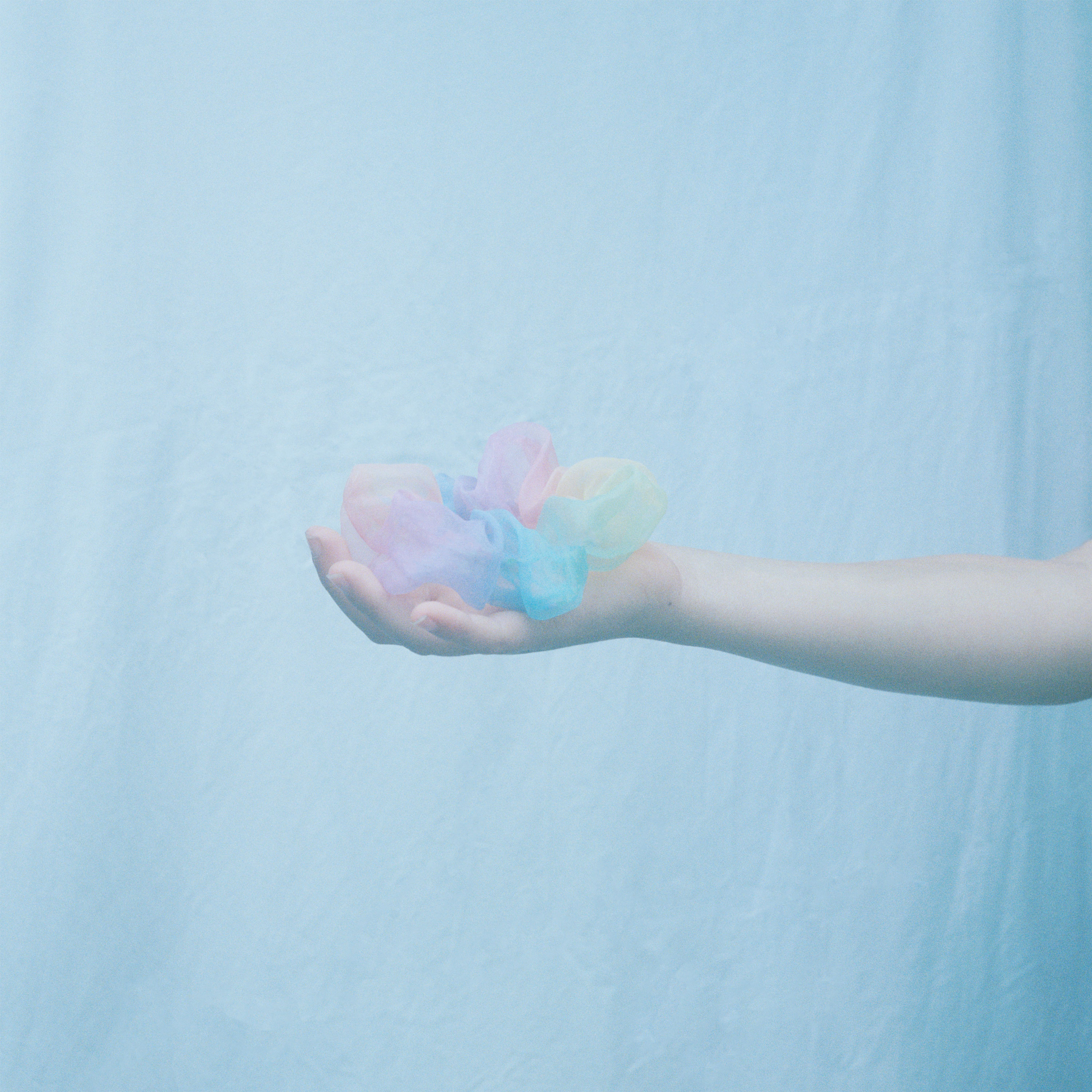 foto i pastellblått med en hand som håller en pastellfärgad hårsnodd