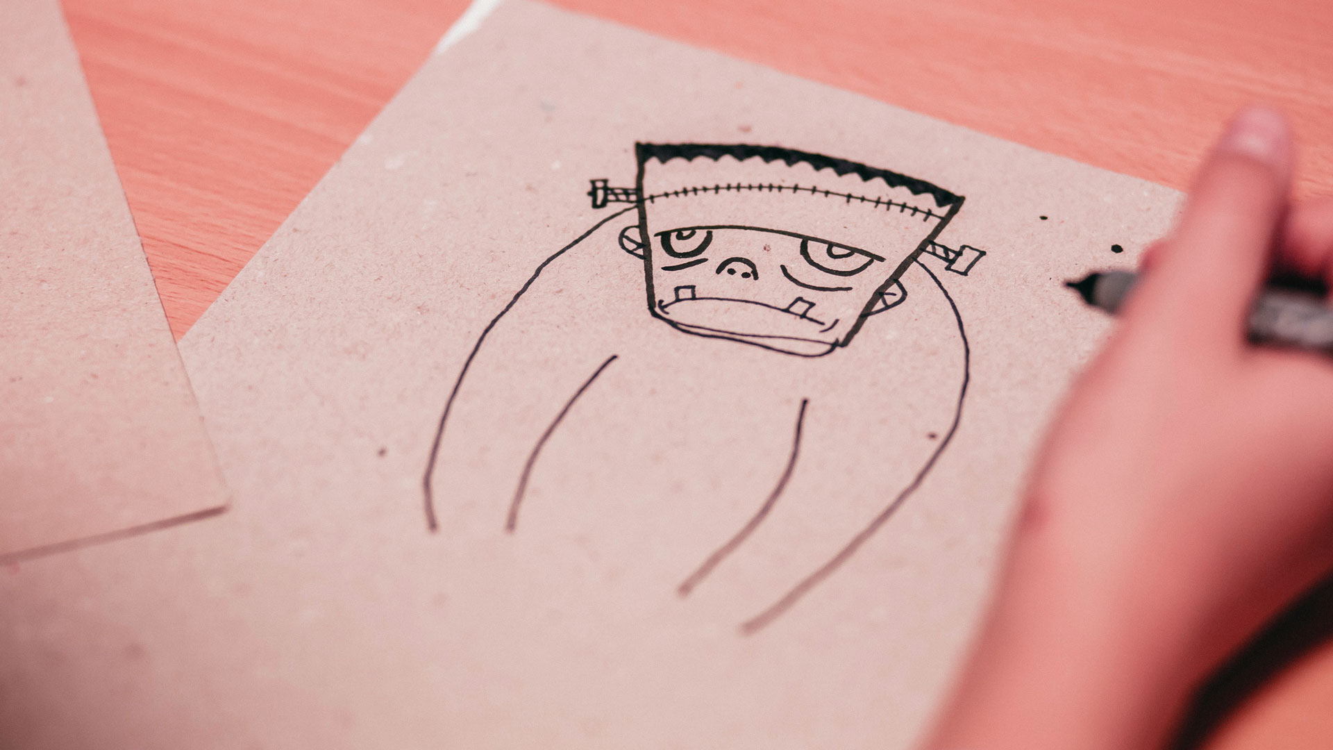 foto av ett barns hand som ritar en seriefigur på ett gråbrunt papper