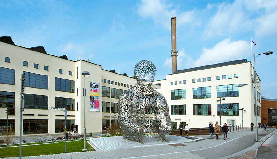 Översiktsfoto av en fabriksbyggnad med en stor skulptur framför föreställandes en människogestalt.