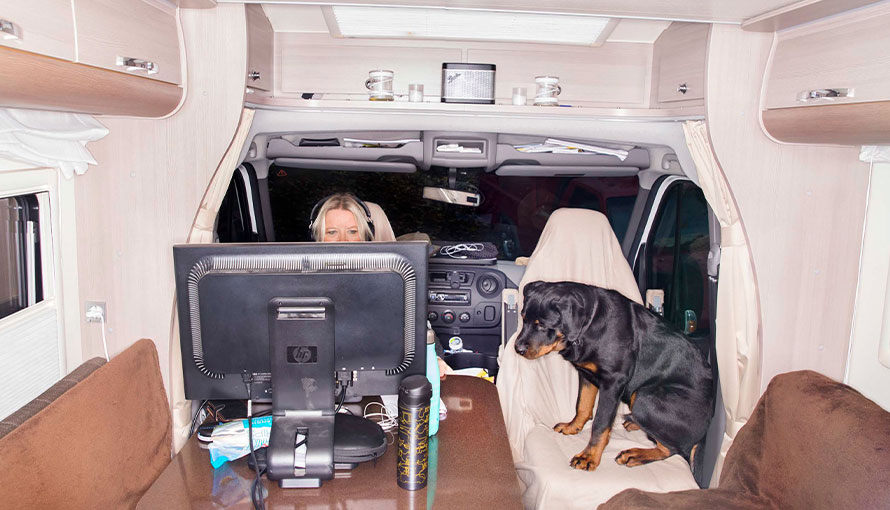 foto av en kvinna i husbil som sitter med hörlurar framför en stor skärm med en stor hund bredvid sig