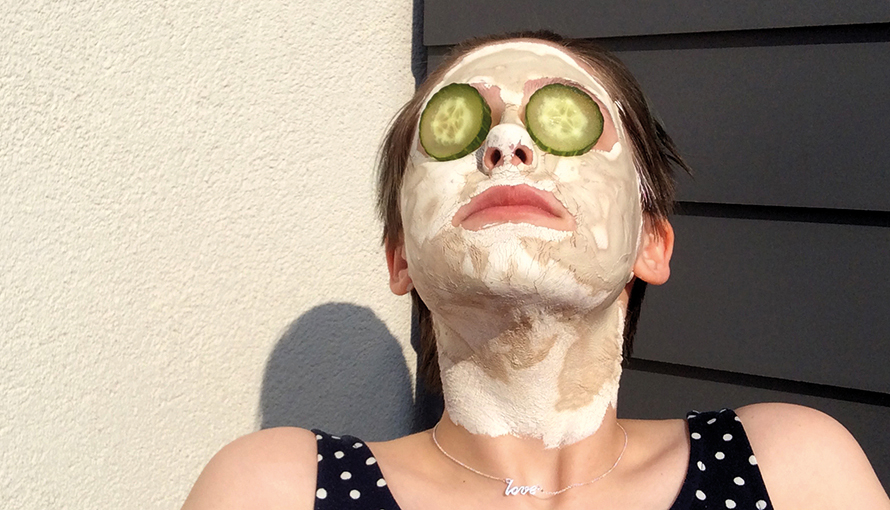 Fotografi på kvinna som solar med ansiktsmask och gurkskivor på ögonen.