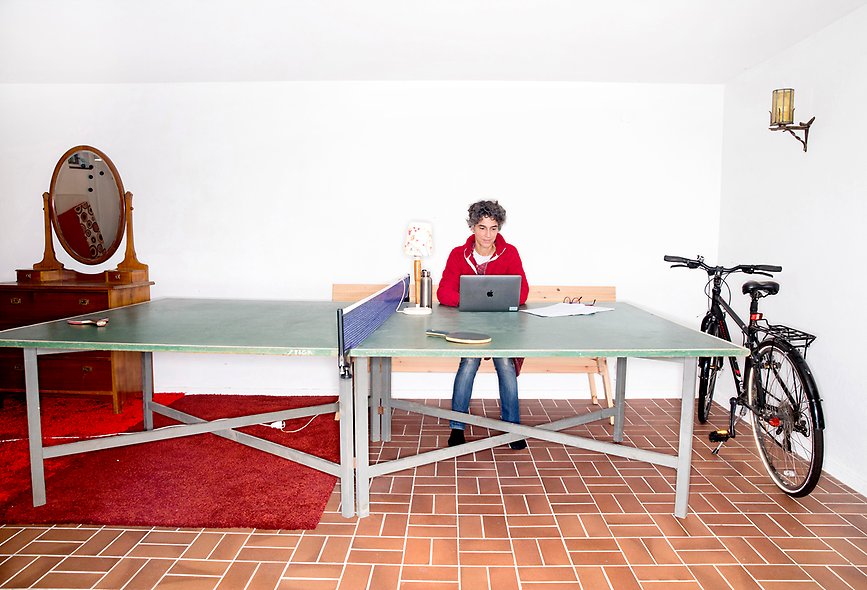foto av en kvinna i kort mörkt hår som sitter framför en laptop placerad på ett pingisbord i en fritidslokal