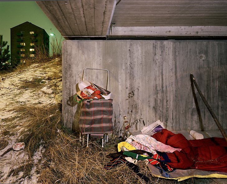 kvällsfoto under en bro där det ligger en sovsäck och rullväska ihop med andra prylar